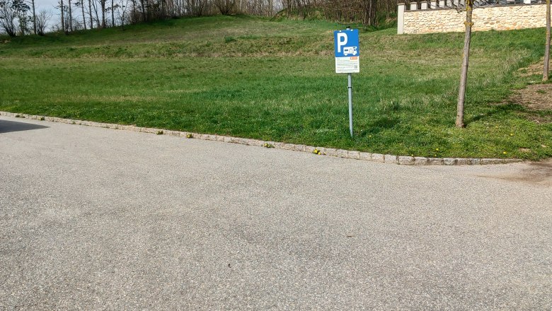Wohnmobilstellplatz Wenzersdorf, © Gemeinde Gnadendorf Parkplatzschild für Wohnmobile auf einem leeren Stellplatz mit Bäumen im Hintergrund.