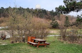 Wohnmobilstellplatz, © Bernhard Zechner Picknicktisch auf einer Wiese mit Bäumen und einem großen weißen Radom im Hintergrund.