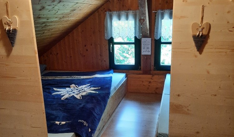 Matratzenlager, © Buschberghütte Ein gemütliches Matratzenlager in einem Dachgeschoss mit Holzverkleidung und zwei Fenstern.