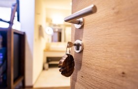 Herzlich Willkommen, © Weinviertel Tourismus GmbH / Herbst Nahaufnahme eines Türgriffs mit Schlüssel und Holzanhänger, unscharfer Hintergrund mit Spiegel.