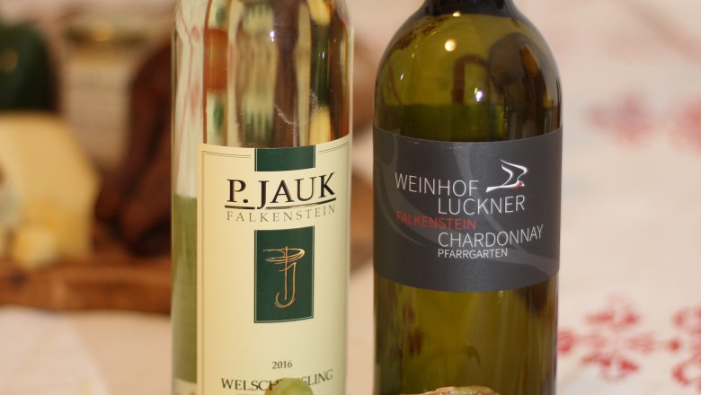 Two bottles of wine and a bunch of green grapes on a table.