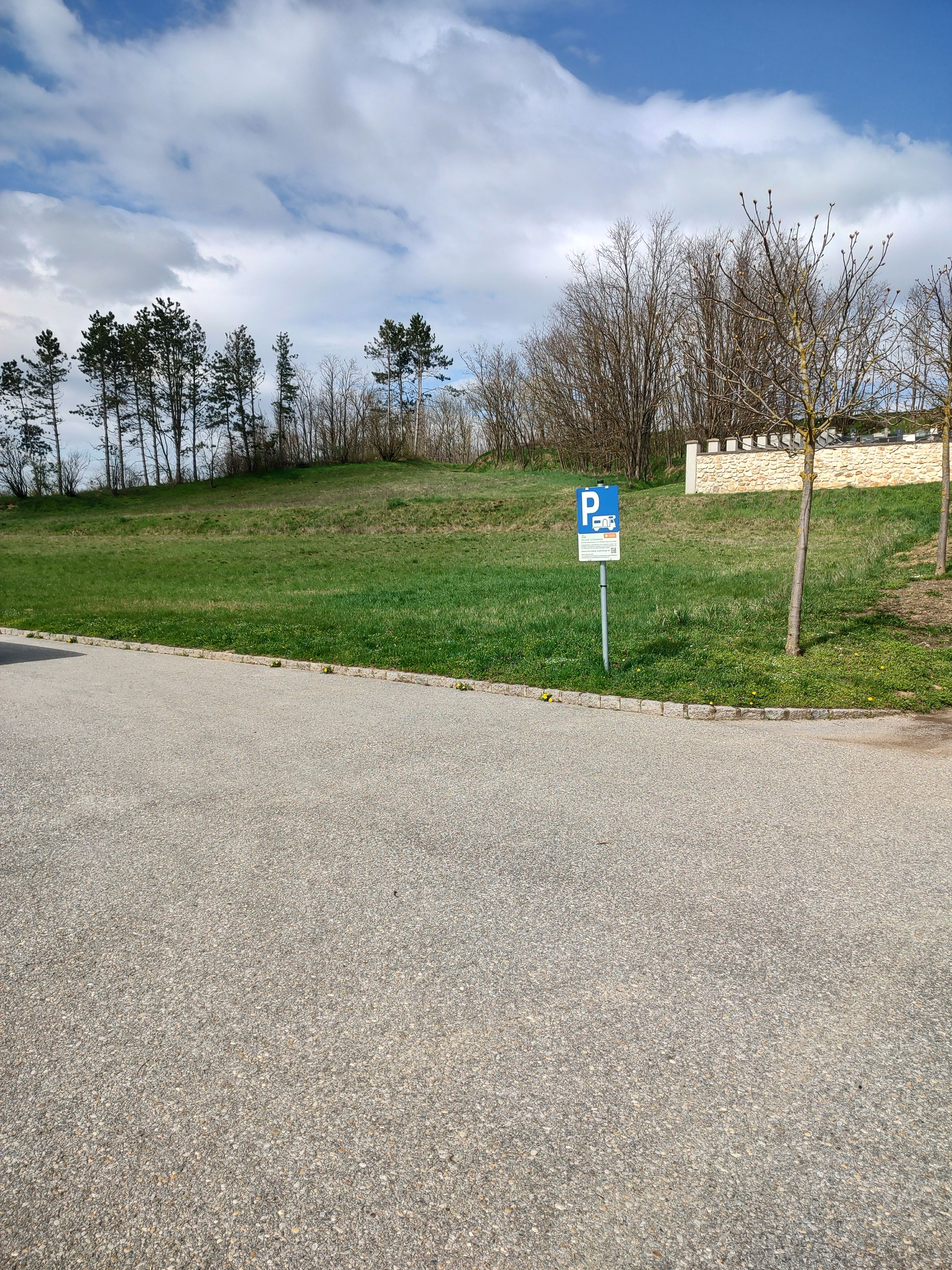 Parkplatzschild für Wohnmobile auf einem leeren Stellplatz mit Bäumen im Hintergrund.