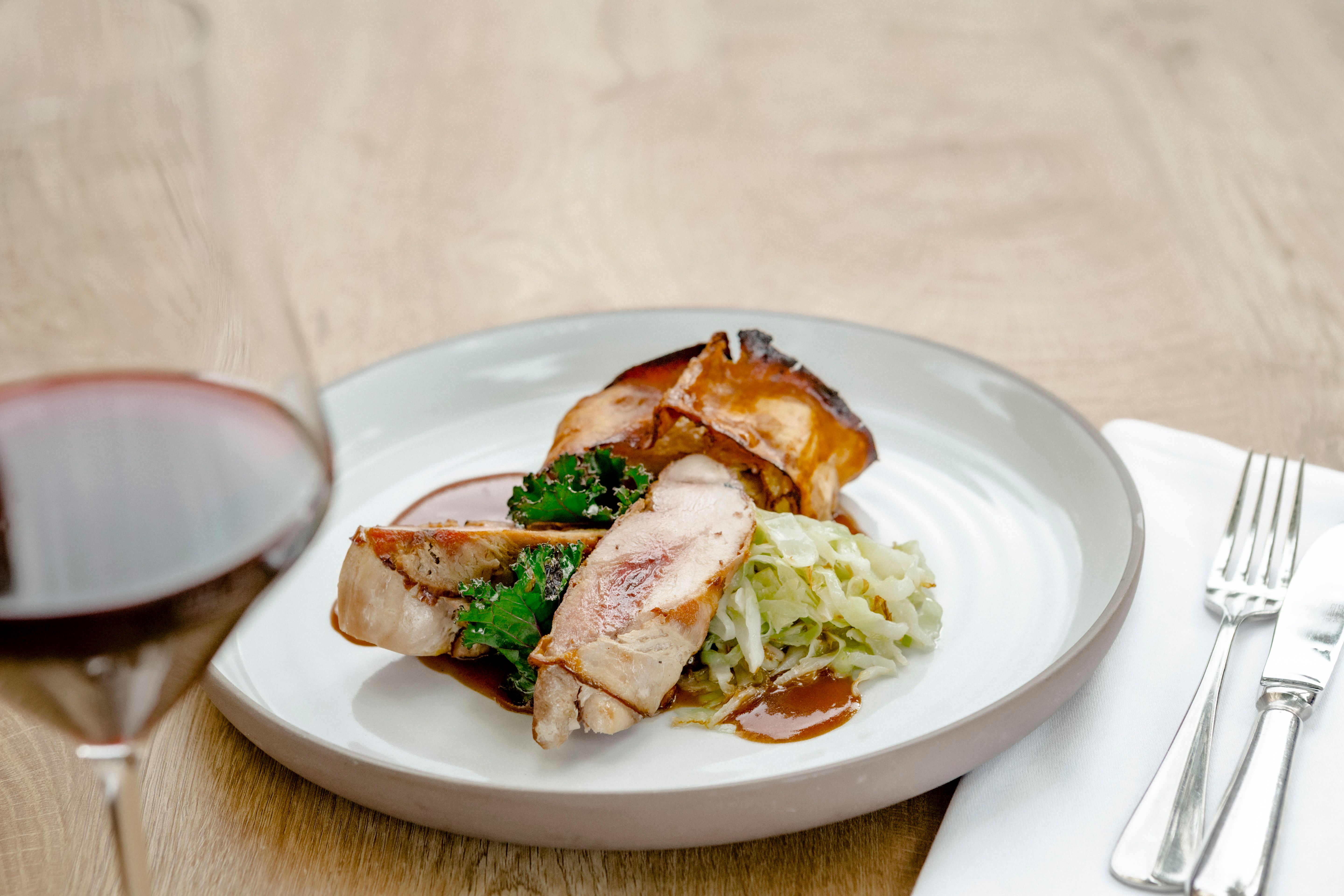 Ein Teller mit Fasanbrust, Grünkohl und Kraut, daneben ein Glas Rotwein.