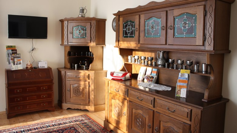 Living room with antique wooden furniture, a TV on the wall and decorative metal vessels.