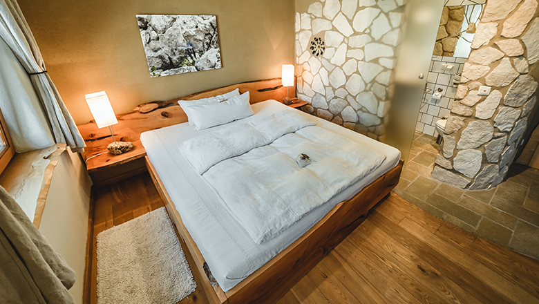 Gemütliches Schlafzimmer mit Holzbett, Steinwänden und modernem Bad.