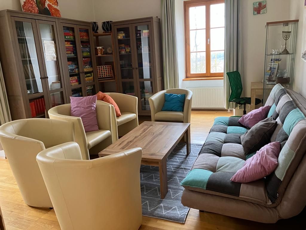 Ein gemütlicher Gemeinschaftsraum mit Sesseln, einem Sofa, einem Tisch und Bücherregalen.