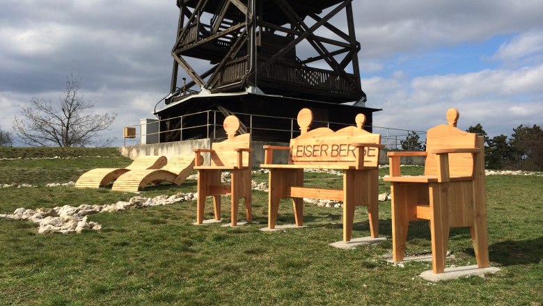 Holzstühle und Liegen vor einem Aussichtsturm im Freien.