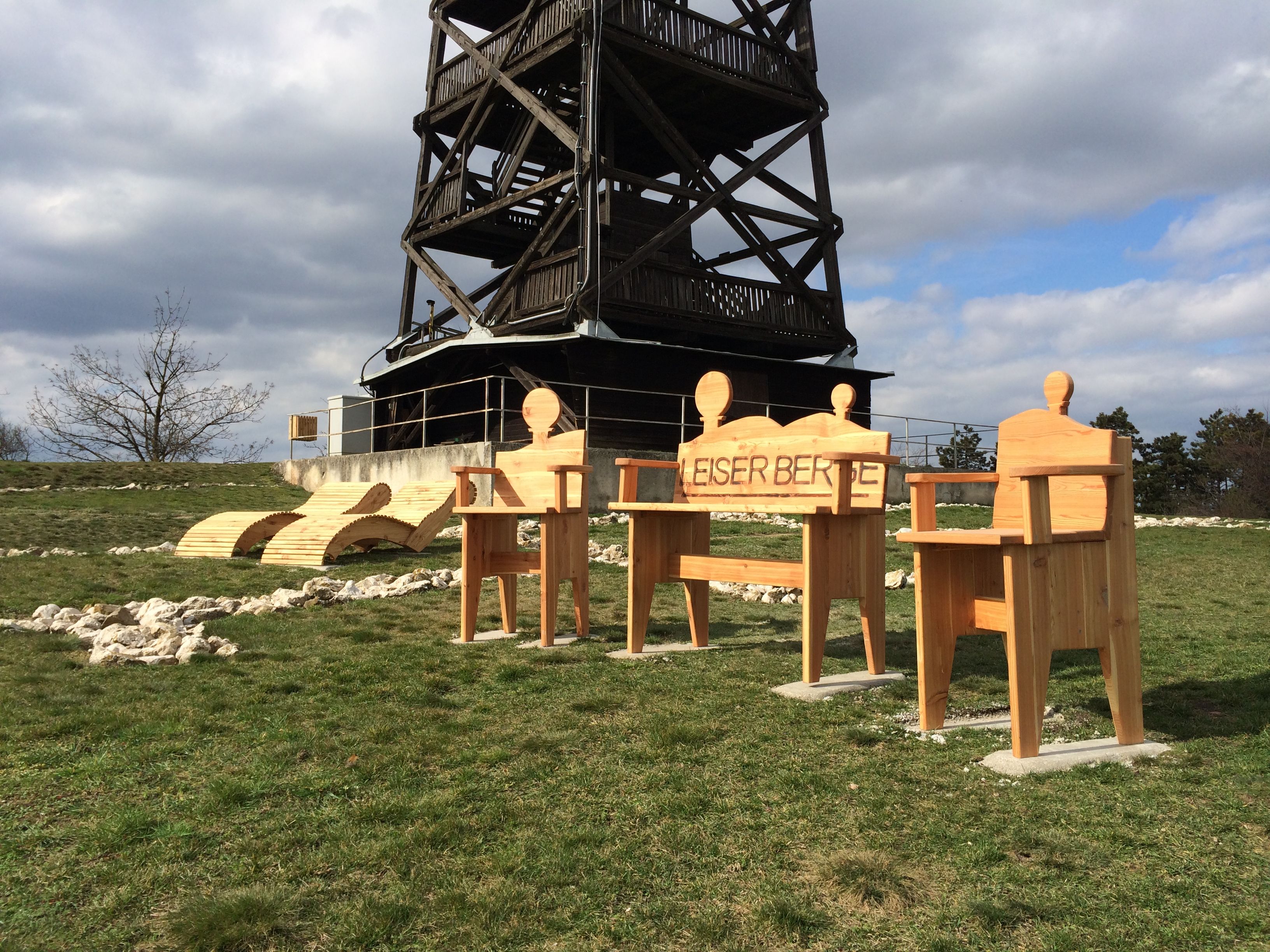 Holzstühle und Liegen vor einem Aussichtsturm im Freien.