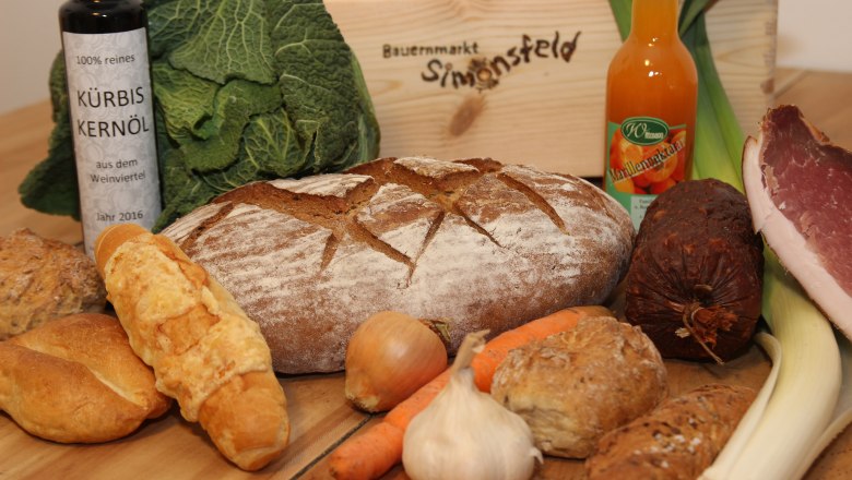 Verschiedene Lebensmittel wie Brot, Gemüse, Öl und Wurst auf einem Tisch.