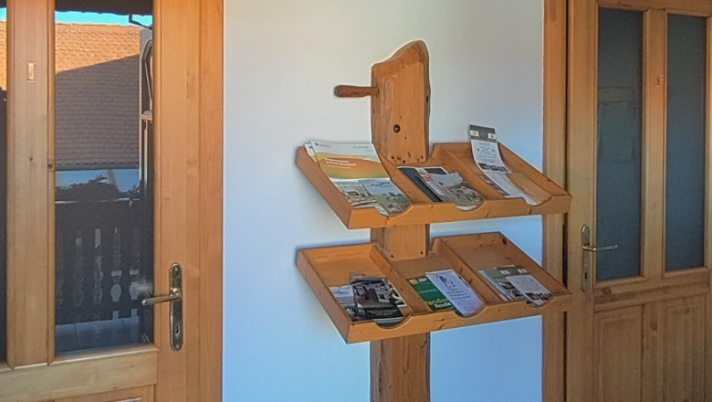 A wooden shelf with brochures on a white wall between two wooden doors.