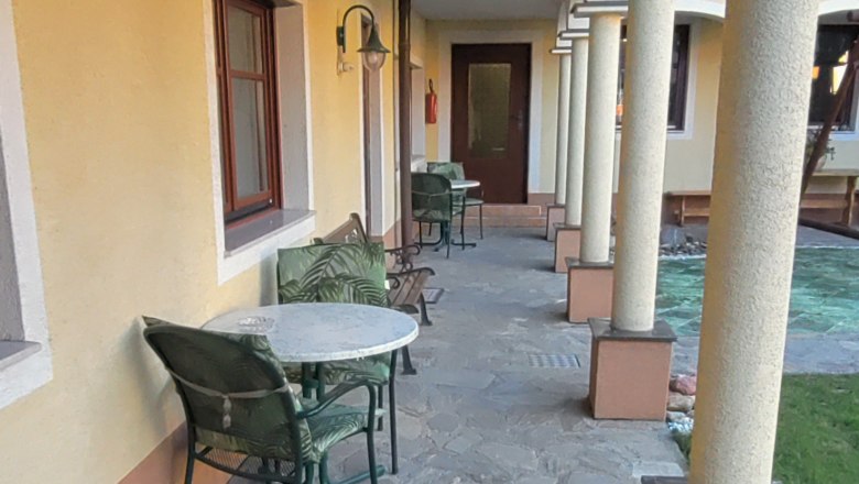 An arcaded courtyard with a stone floor, yellow wall and columns. Tables and chairs are placed along the wall.