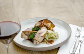 Ein Teller mit Fasanbrust, Grünkohl und Kraut, daneben ein Glas Rotwein.