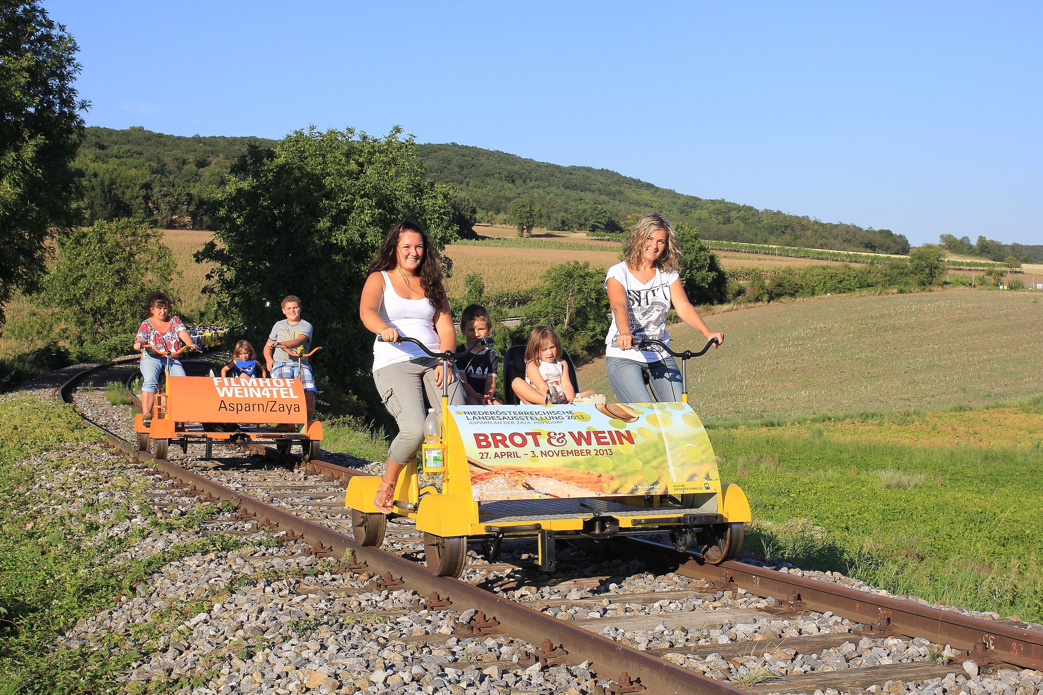 Menschen fahren auf Draisinen durch eine ländliche Landschaft.