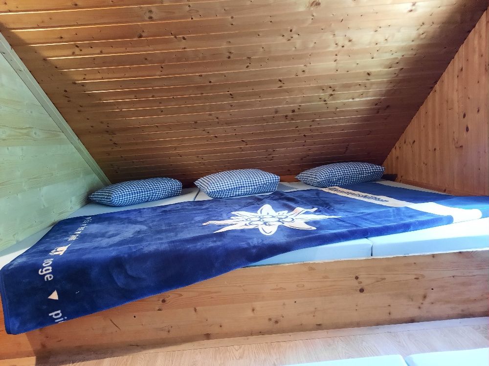 Ein Matratzenlager mit blauer Decke und karierten Kissen unter einer Holzdecke.