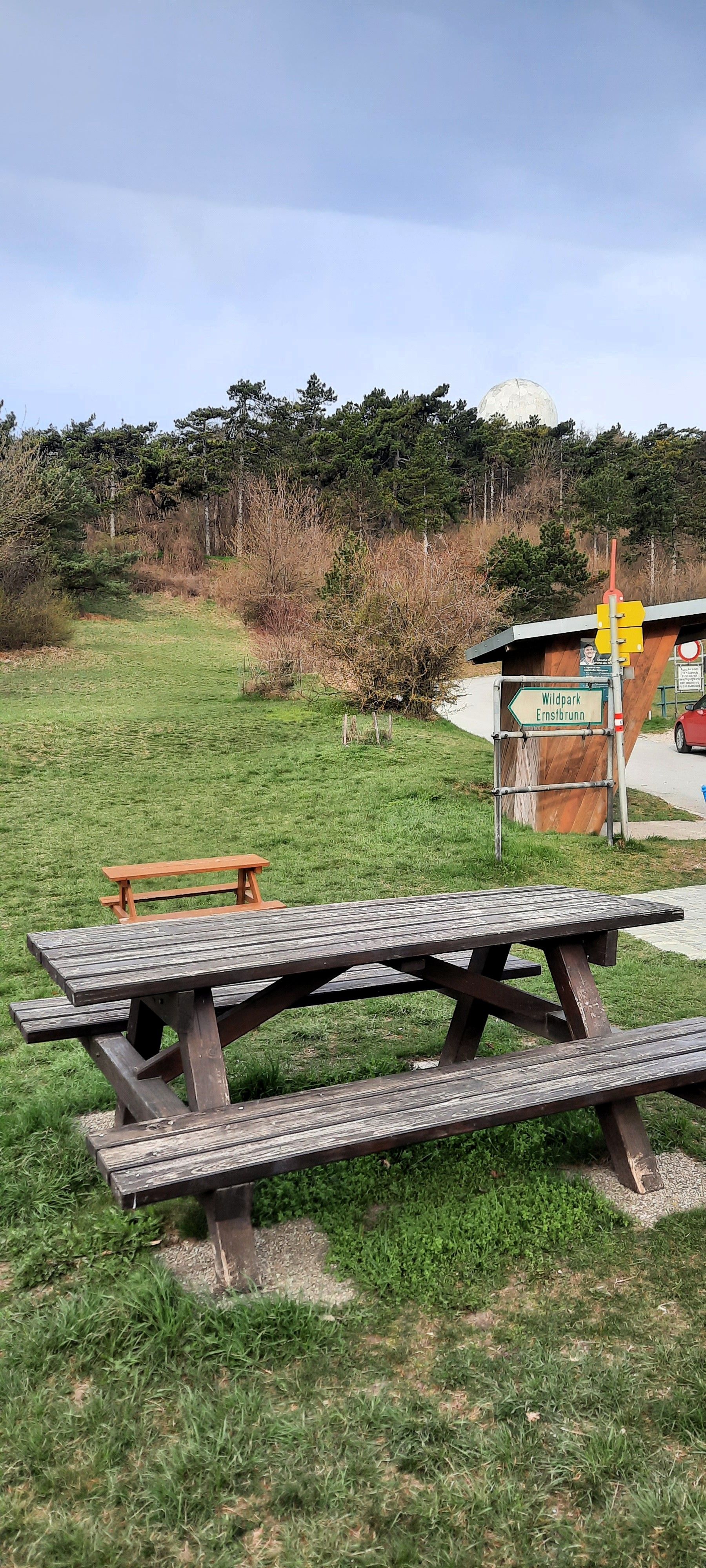Picnic table on a meadow with a forest in the background and a sign for Ernstbrunn Wildlife Park.