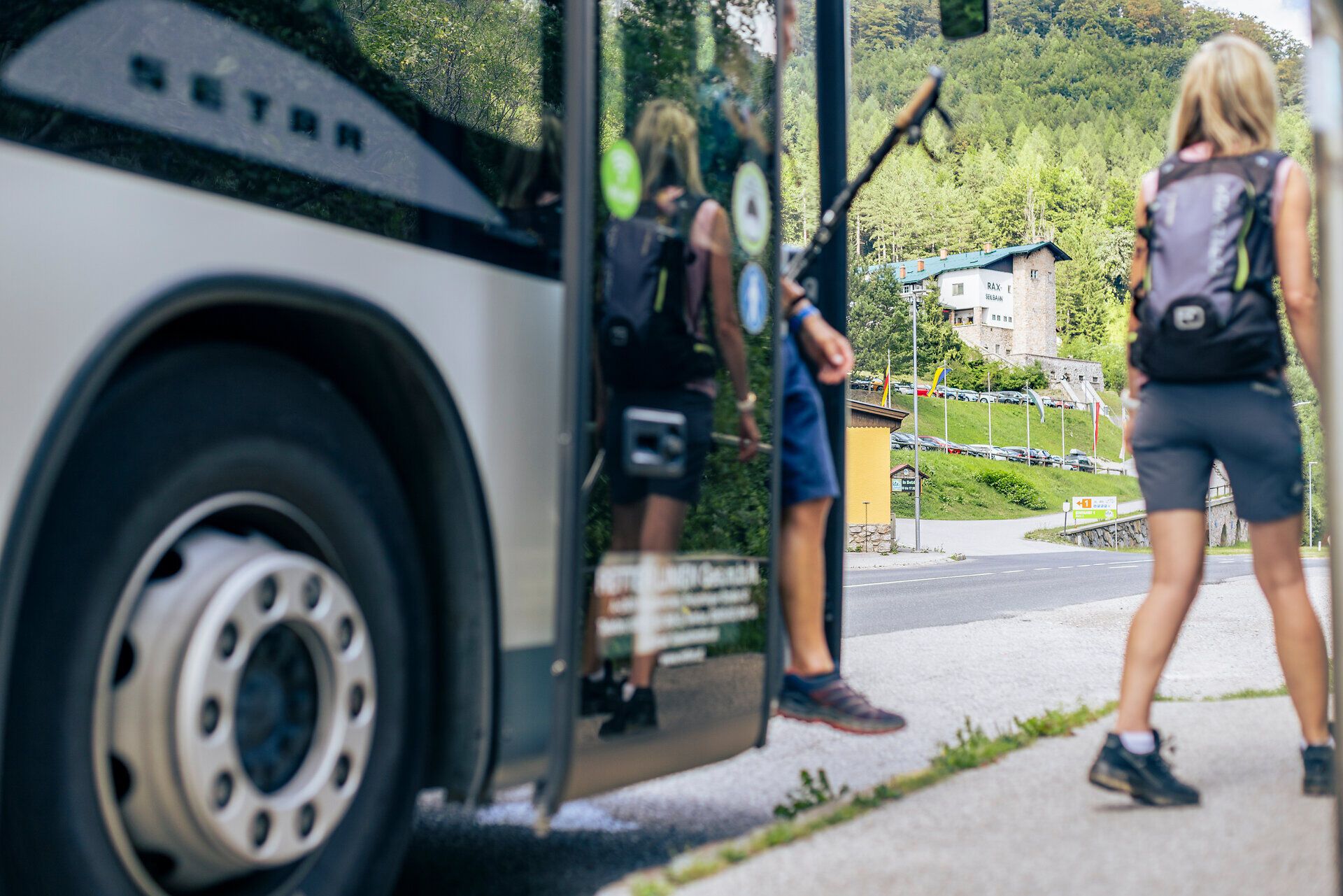Wandernde steigen mit Rucksäcken an einer Haltestelle aus einem Bus aus.