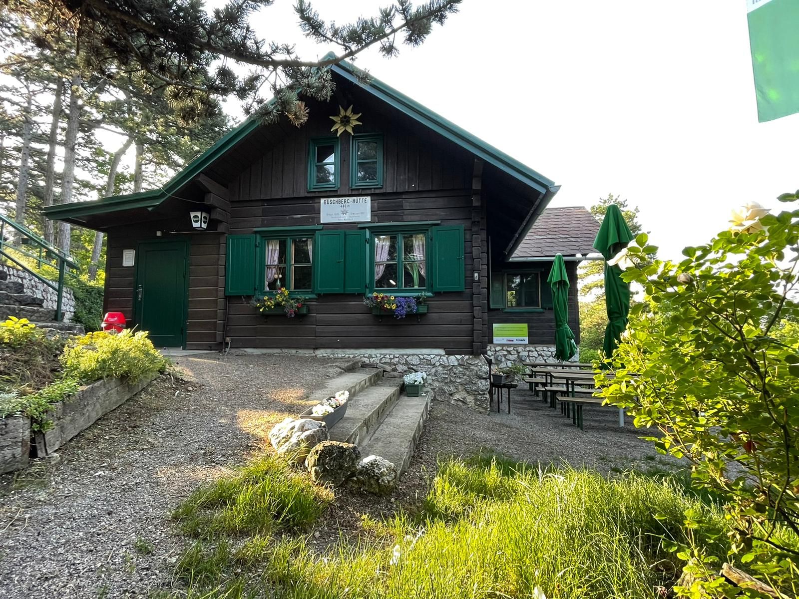 Eine rustikale Holzhütte mit grünen Fensterläden und Blumenkästen, umgeben von Bäumen und Gartenmöbeln.