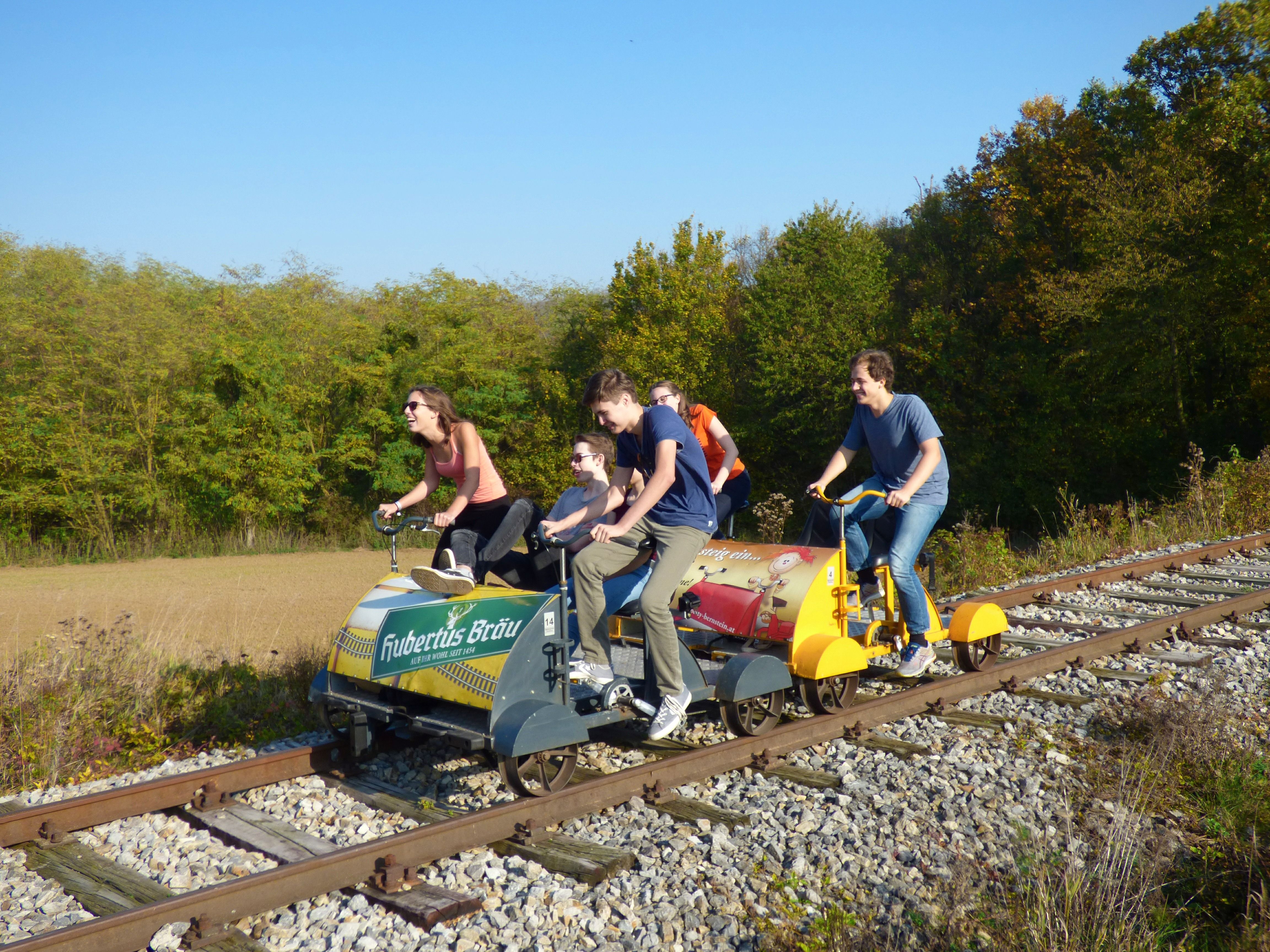 Gruppe von Menschen fährt auf einer Draisine auf Bahngleisen durch eine ländliche Landschaft.