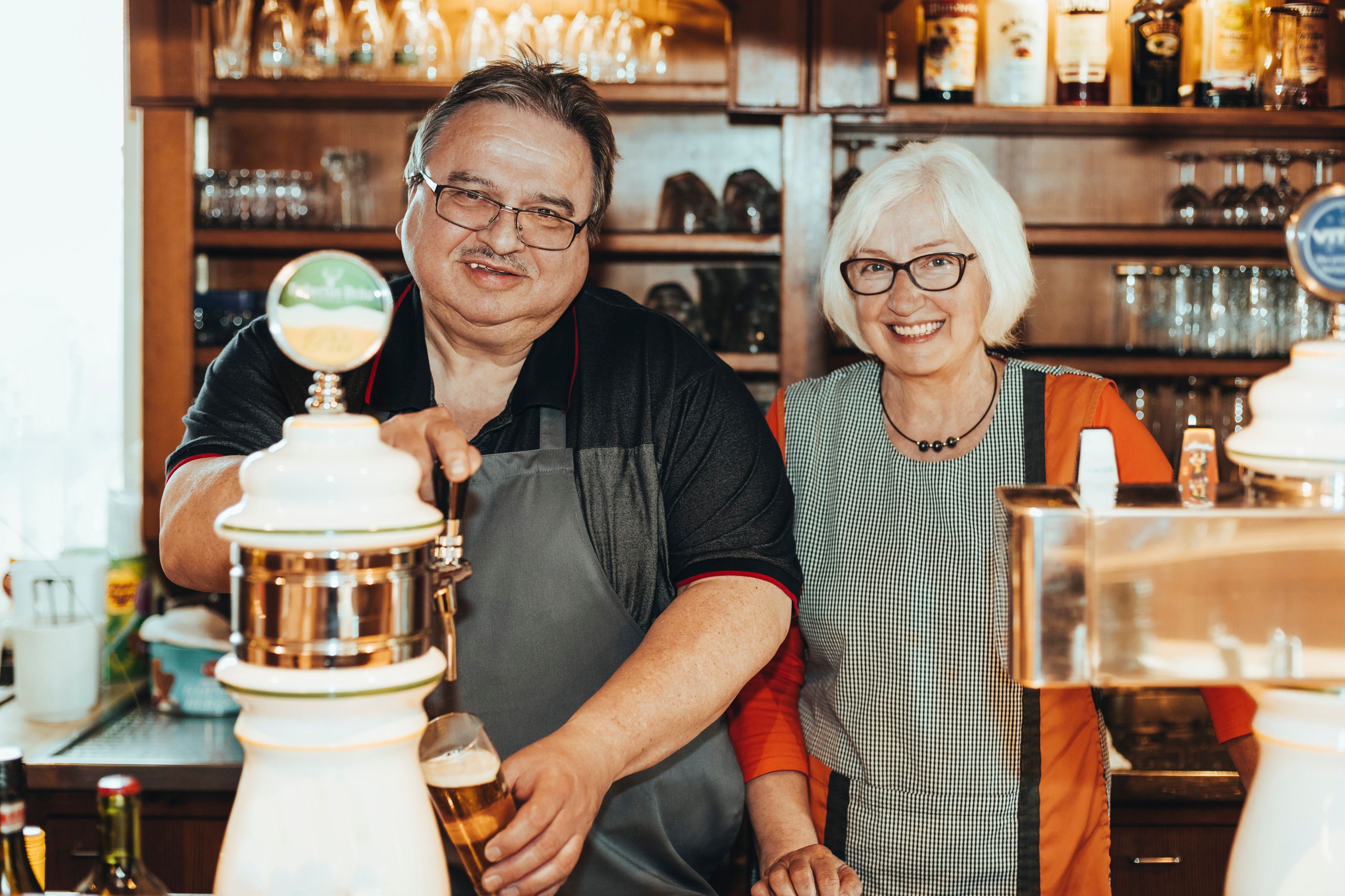 Zwei Personen hinter einer Bar, eine Person zapft Bier.