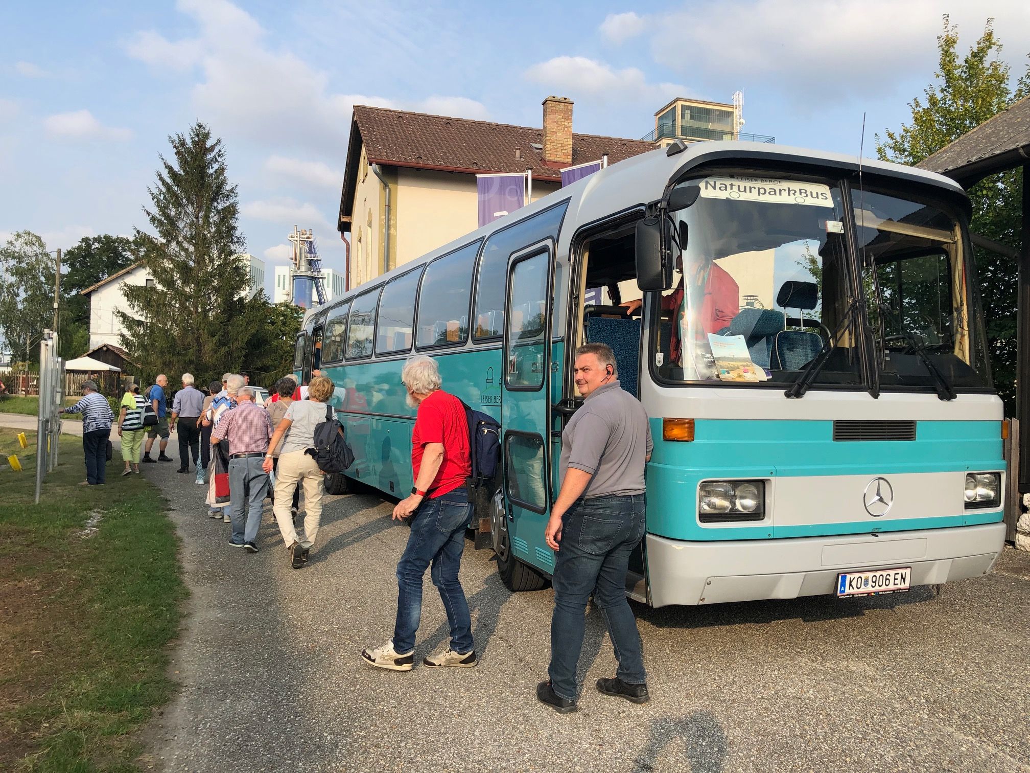 Eine Gruppe von Menschen steigt in einen türkisfarbenen Bus mit der Aufschrift 'NaturparkBus' ein.