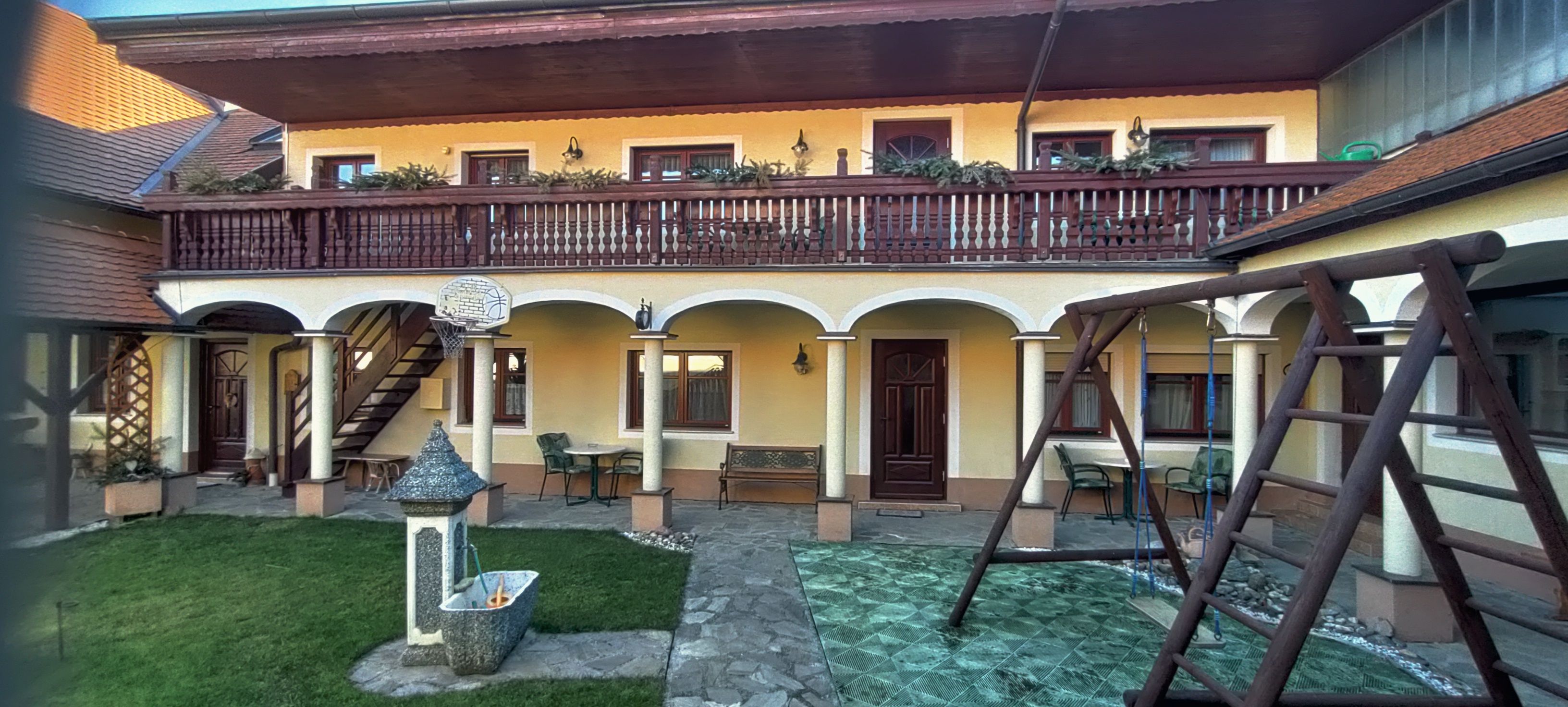 Innenhof mit Arkaden, Balkon, Schaukel und Brunnen.