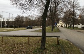 Parkplatz mit B&auml;umen und einem Geb&auml;ude im Hintergrund.