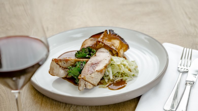 Ein Teller mit Fasanbrust, Grünkohl und Kraut, daneben ein Glas Rotwein.