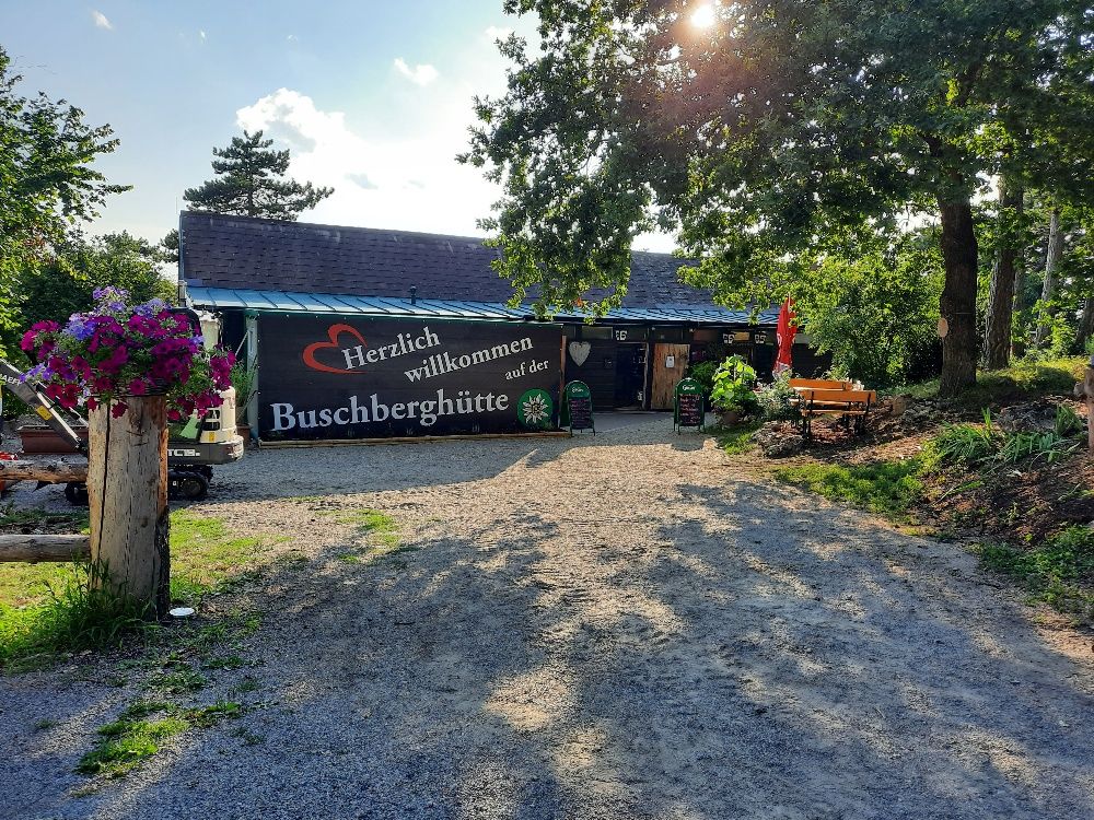 Eingangsbereich der Buschberghütte mit Willkommensschild und Blumen.
