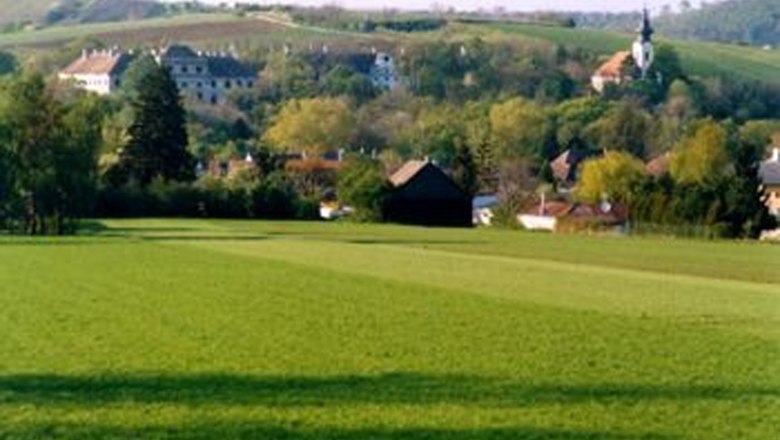 Grüne Wiesen mit Dorf und Kirche im Hintergrund.
