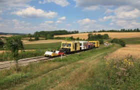 Draisines on a rural railroad line in a hilly landscape with fields and trees.