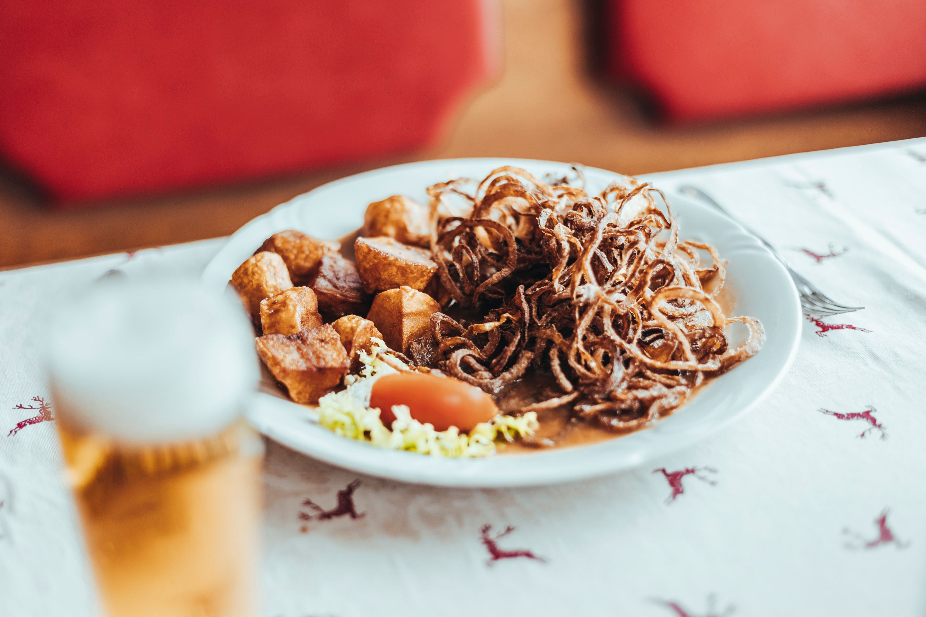 Ein Teller mit Zwiebelrostbraten, Braterdäpfeln und Salat auf einem Tisch mit Hirschmuster.