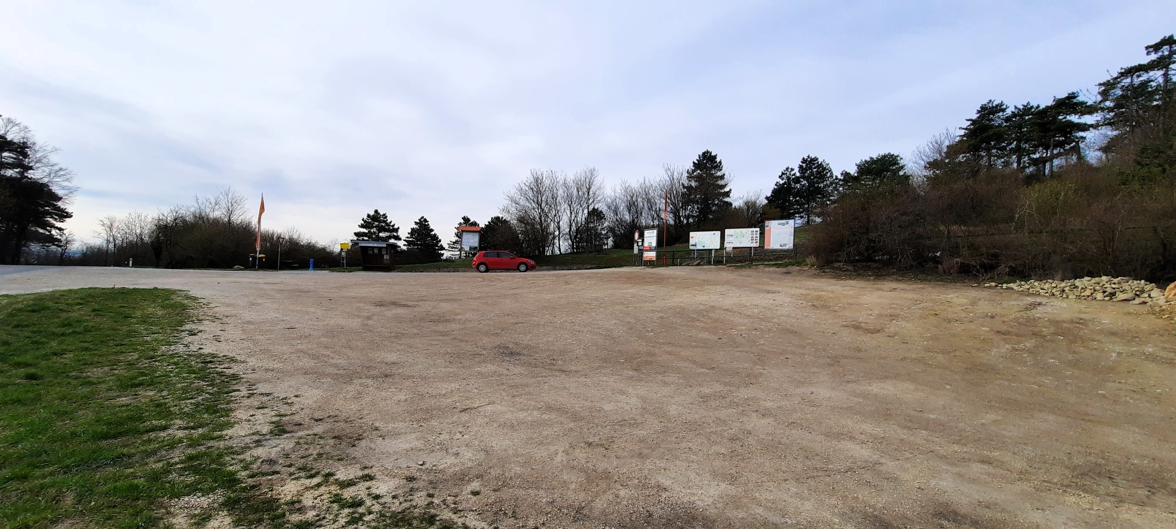 Empty camper van site with a red car and trees in the background.