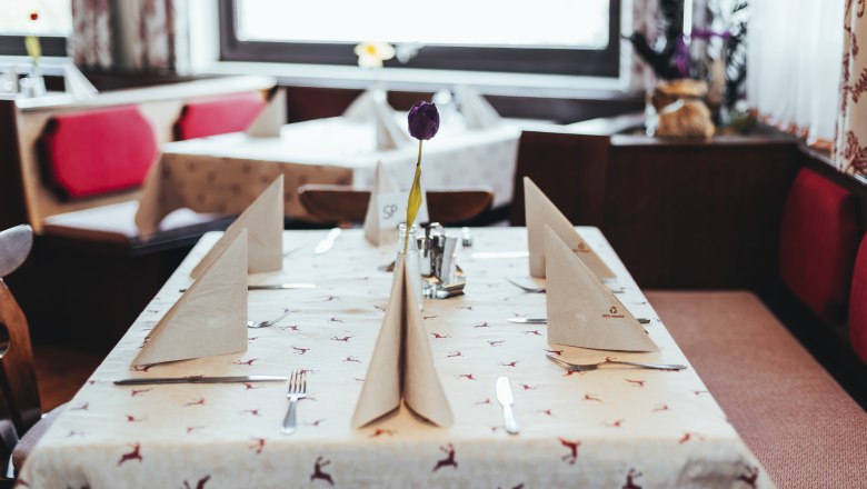 A table set in an inn with folded napkins and a purple flower in the center.