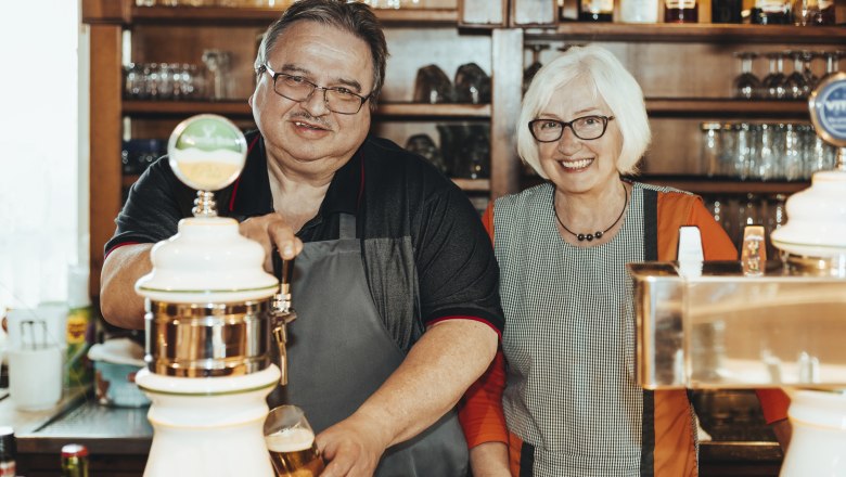 Two people behind a bar, one person tapping beer.