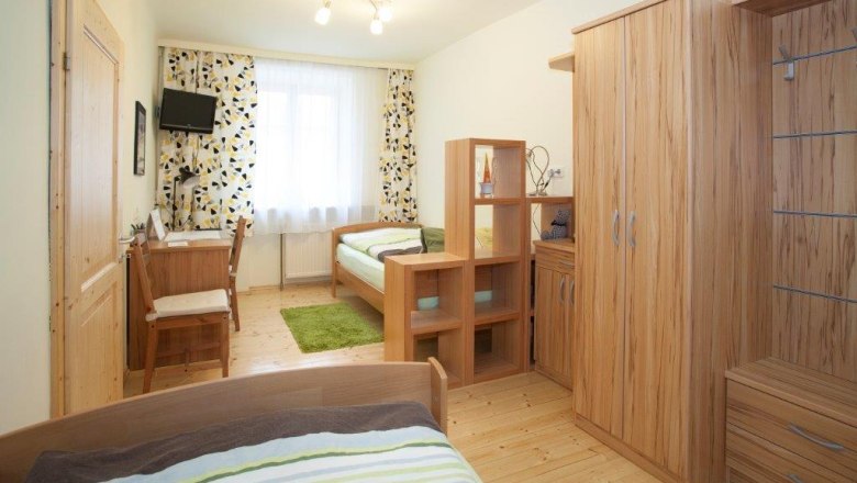 Ein helles Schlafzimmer mit Holzmöbeln, zwei Betten, einem Schreibtisch und einem kleinen Fernseher an der Wand.