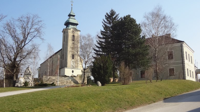 Kirche mit Turm und angrenzendem Gebäude in Gnadendorf, umgeben von Bäumen und Rasenfläche.