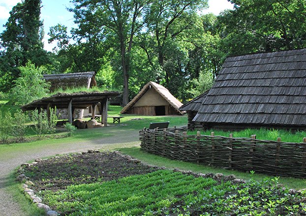 Historical replica of a village with wooden huts and garden.