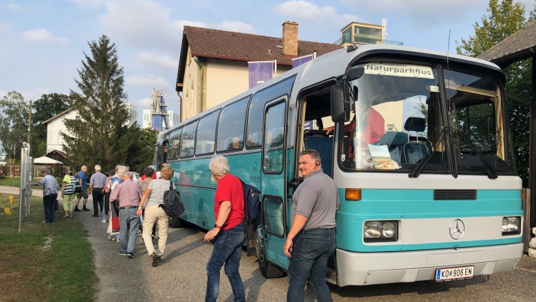 A group of people board a turquoise-colored bus with the sign 'NaturparkBus'.