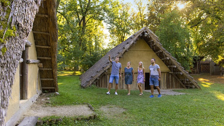 Four people stand outside a historic building with a thatched roof.