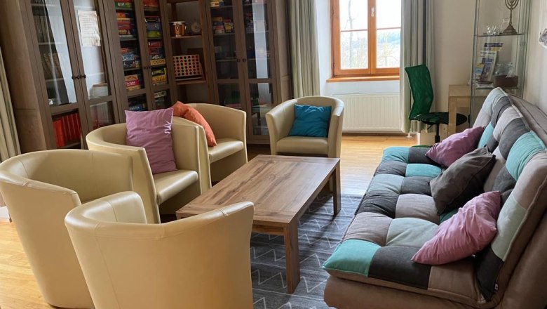 A cozy common room with armchairs, a sofa, a table and bookshelves.