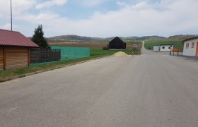 Ein leerer Parkplatz mit umliegenden Geb&auml;uden und Feldern im Hintergrund.