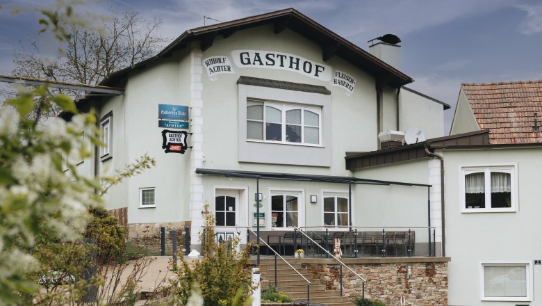 Au&szlig;enansicht eines Gasthofs mit Terrasse und Treppe, umgeben von Pflanzen.