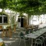 A covered outdoor area with tables and chairs under a vine arbor.