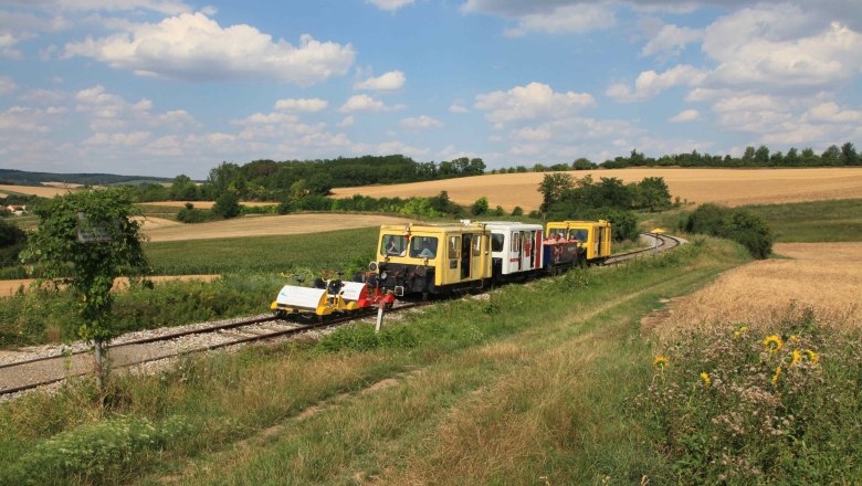 Draisines on a rural railroad line in a hilly landscape with fields and trees.