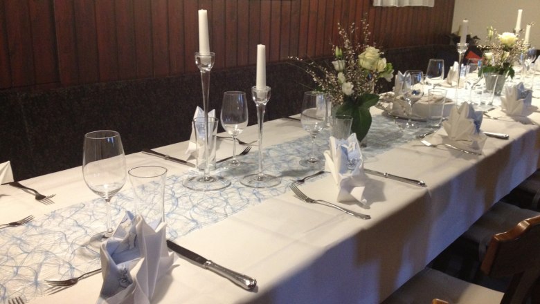 Elegant, festively laid table with white tablecloths, candles and flower arrangements.
