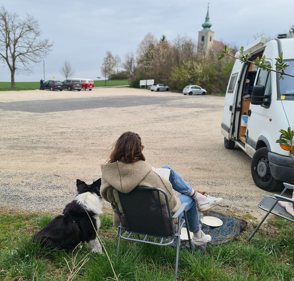 Dame mit Hund neben weißen Campingbus und Blick auf Oberleiserberg mitK Kirche