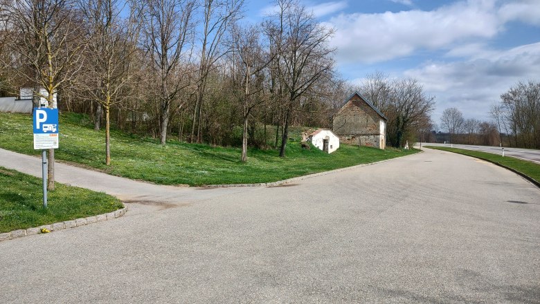 Wohnmobilstellplatz Wenzersdorf, © Gemeinde Gnadendorf Parkplatz mit Wohnmobilstellplatzschild, Bäume und altes Gebäude im Hintergrund.