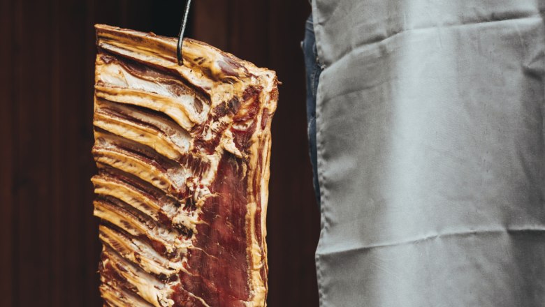 Person holds a large piece of meat with ribs on a hook.