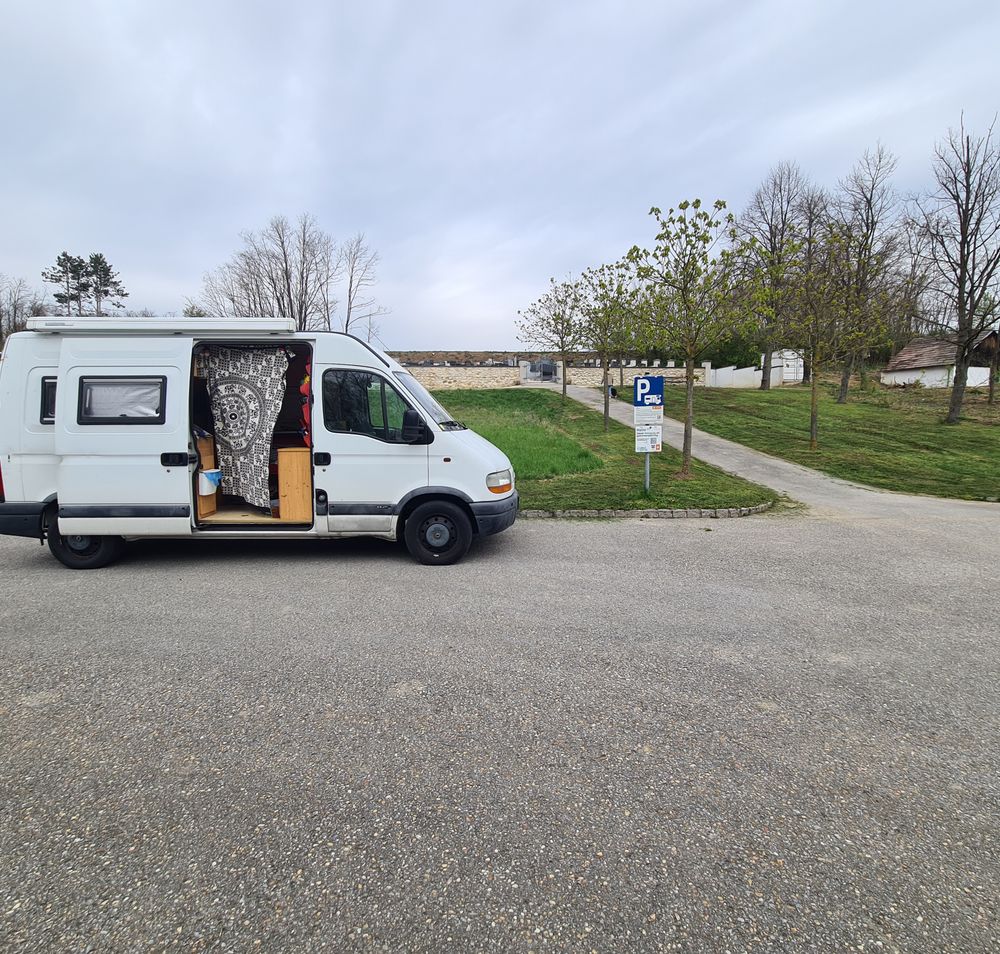 weißer Camper auf Stellplatz vor Weg zum Friedhof, umgeben von Feldern