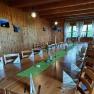 A rustic room with wooden walls and ceiling. A long table is set with a green tablecloth, candles and folded napkins.